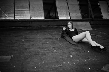 Sexy model girl wit long legs at black lingerie outfit body swimsuit combidress and jacket posed at the roof of abadoned industrial place with windows.