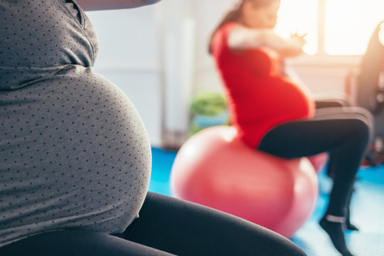 Closeup of a pregnant women sitting on Pilates ball stretching