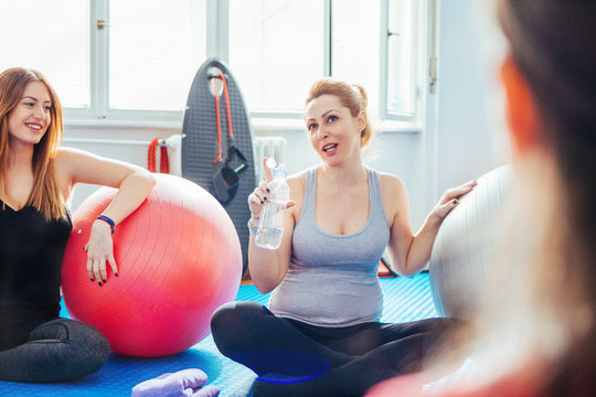 Smiling pregnant women relaxing after Pilates training and talking