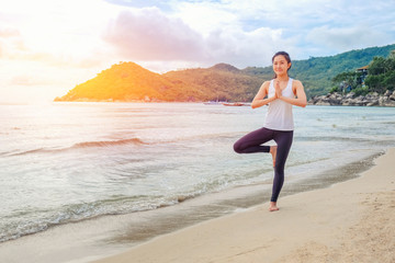 Young beautiful woman practicing yoga on the beach at sunlight