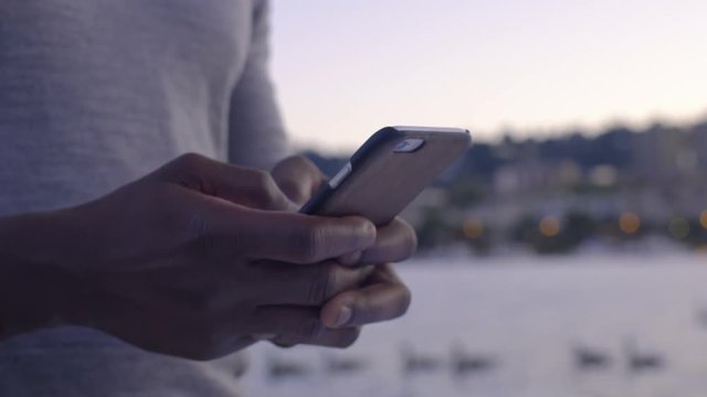 Closeup of Man's Hands Texting On Smartphone, Beautiful River And Cityscape In Background