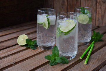 Glass of cold homemade lemonade or mojito cocktail with lime and mint on wooden background. Soda drink. Copy space