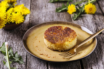 Pieces of simple homemade semolina sponge cake with saffron on vintage wooden table decorated dandelions. Selective focus 
