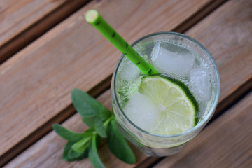 Glass of cold homemade lemonade or mojito cocktail with lime and mint on wooden background. Soda drink. Copy space