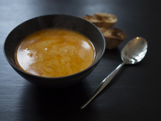 Hot crab bisque in black ceramic bowl with pieces of grilled bread and a spoon on black background