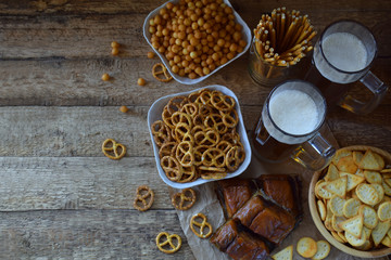 Football fan set with mugs of beer and salty snacks on wooden background. Crackers, pretzel, salted straws, nuts, dried fish. Junk food for beer or cola. Photographed with natural light