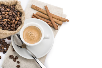 cup of coffee on napkin with canvas bag full of coffee beans and cinnamon, on white background