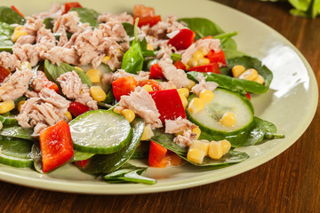 Fresh spinach salad with tuna, cucumber, corn, and red paprika on a plate