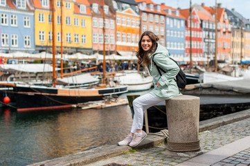 Happy young tourist woman with backpack at Copenhagen, Nyhavn, Denmark. Visiting Scandinavia, famous European destination during fall or spring. Travel and Lifestyle. 