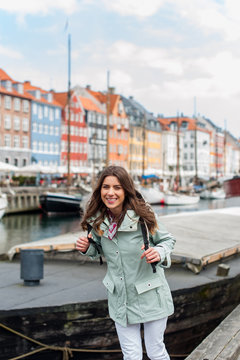 Happy young tourist woman with backpack at Copenhagen, Nyhavn, Denmark. Visiting Scandinavia, famous European destination during fall or spring. Travel and Lifestyle. 