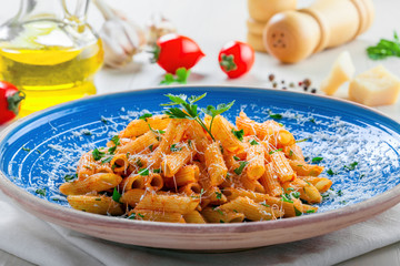 Traditional Italian penne pasta with arrabiata tomato sauce on a blue rustic plate. Delicious healthy Mediterranean cuisine food. Close-up.