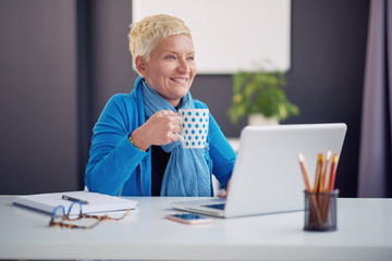 Businesswoman using laptop and drinking coffee while sitting in modern office