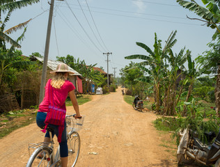 Myanmar Tourist Bike Ride. Women riding a bicycle through a rural farming village near Nyaung Shwe, Inle Lake, Myanmar.