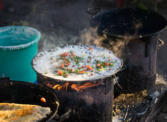 Burmese Street Snack. Pancake with chick peas, tomato and spring onion baking on a fire stove. Scene from Kyaukme night market, Shan State, Myanmar.