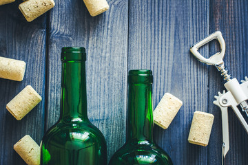 Green empty wine bottles and white wine opener on blue wooden table background.