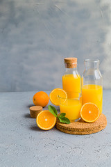 Fresh Orange Juice in Glass and Bottles and some Ripe Oranges on Grey Background. Healthy Drink, diet or Detox. © shutnica