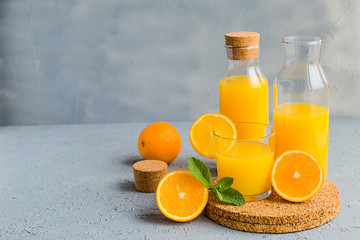 Fresh Orange Juice in Glass and Bottles and some Ripe Oranges on Grey Background. Healthy Drink, diet or Detox. © shutnica