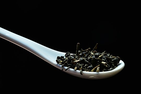Mixture of dried leaves of green tea  Camellia sinensis and morrocan mint Metha Spicata Nana on white laboratory ceramic spoon, black background