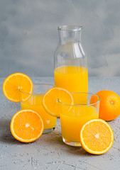 Fresh Orange Juice in Glass and Bottles and some Ripe Oranges on Grey Background. Healthy Drink, diet or Detox.