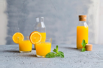 Fresh Orange Juice in Glass and Bottles and some Ripe Oranges on Grey Background. Healthy Drink, diet or Detox. © shutnica