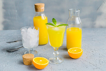 Fresh Orange Juice in Glass and Bottles and some Ripe Oranges on Grey Background. Healthy Drink, diet or Detox.