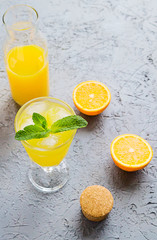 Fresh Orange Juice in Glass and Bottles and some Ripe Oranges on Grey Background. Healthy Drink, diet or Detox.