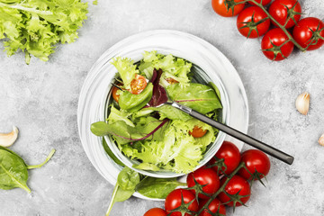 The dietary mixed greens salad (mesclun, mache, lettuce) and cherry tomatoes in a bowl on a light background. Top view. Food background