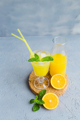 Fresh Orange Juice in Glass and Bottles and some Ripe Oranges on Grey Background. Healthy Drink, diet or Detox.