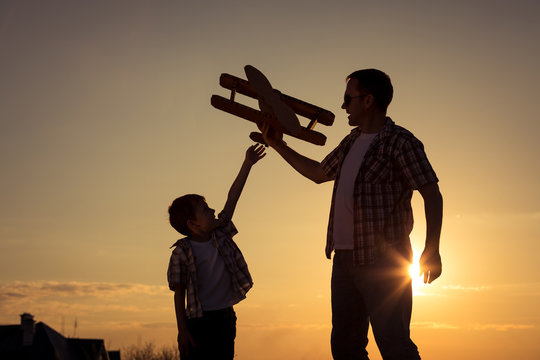 Father and son playing with cardboard toy airplane in the park at the sunset time.