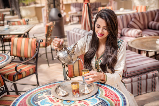 Arab Woman pouring tea. Middle Eastern arab woman in traditional  Moroccan dress drinking Moroccan Tea. Ramadan holiday theme.