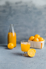 Fresh Orange Juice in Glass and Bottles and some Ripe Oranges on Grey Background. Healthy Drink, diet or Detox. © shutnica