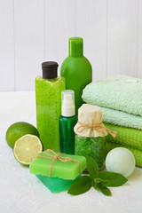 Lime mint composition of beauty threatment products in green colors on a white concrete background: shampoo, soap, bath salt, towel, oil. Various bath accessories. Items for the spa.