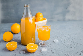 Fresh Orange Juice in Glass and Bottles and some Ripe Oranges on Grey Background. Healthy Drink, diet or Detox. © shutnica