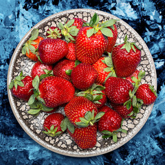 fresh ripe useful fruit strawberry in a clay bowl closeup on a marble dark blue background