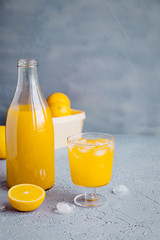 Fresh Orange Juice in Glass and Bottles and some Ripe Oranges on Grey Background. Healthy Drink, diet or Detox.