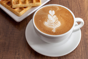 Coffee cup of latte art  beside with waffles on wooden background