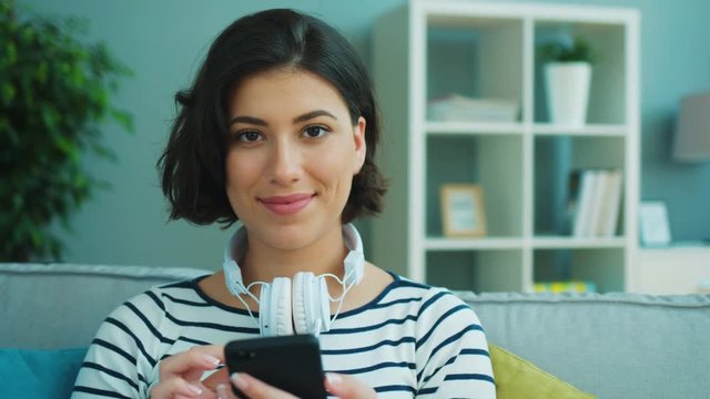 Attractive woman wearing headphones using smart phone while sitting on the couch at home. Portrait shot