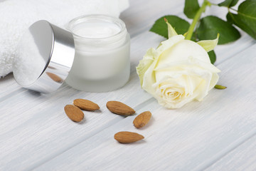 Close-up of a pot of cream for the skin, towel, a white rose and almonds on wooden table.