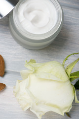 Close-up of a pot of cream for the skin, white rose and almonds on wooden table. Vertical shoot.