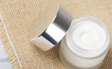 Close-up of a pot of skin cream on brown rustic fabric. Horizontal shoot.