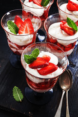 Homemade layered  dessert with fresh strawberry, mascarpone cheese in vintage glasses on old black board.