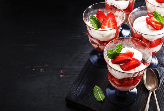 Homemade layered  dessert with fresh strawberry, mascarpone cheese in vintage glasses on old black board.