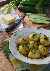 Organically grown new potatoes with butter and dill on wooden background. First spring harvest.