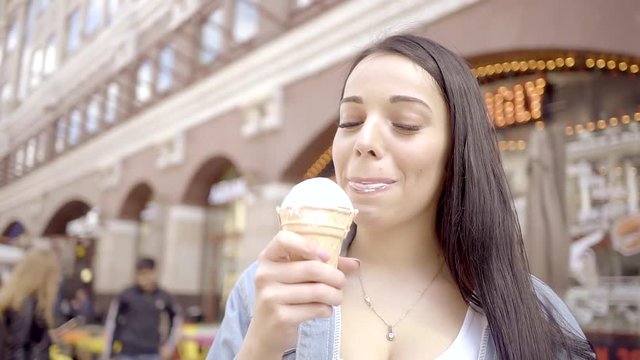 Young charming girl eats white vanilla ice cream cone on the street and happy
