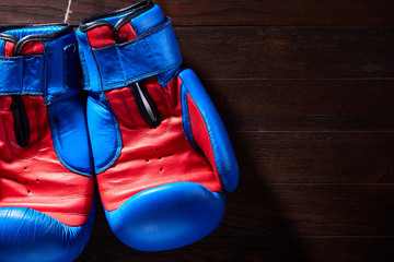 Boxing blue and red gloves hanging from ropes on a wooden background.