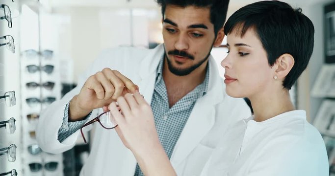 Beautiful woman with optician trying eyeglasses at optics store