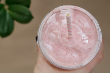 Hand holding a strawberry smoothie in a plastic cup with a straw. Summer & healthy lifestyle concept.