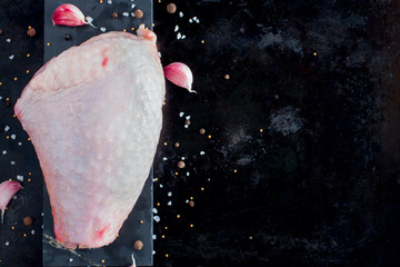 Fresh raw turkey thigh meat on a black background with spices and salt, top view, copy space