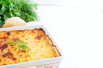 Potato gratin in ceramic form on a white table, horizontal, copy space