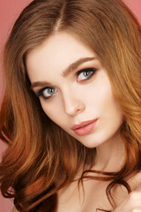 Naklejka premium Red hair girl with long and shiny wavy hair . Beautiful model with curly hairstyle wearing colorful bracelet. Pink background.
